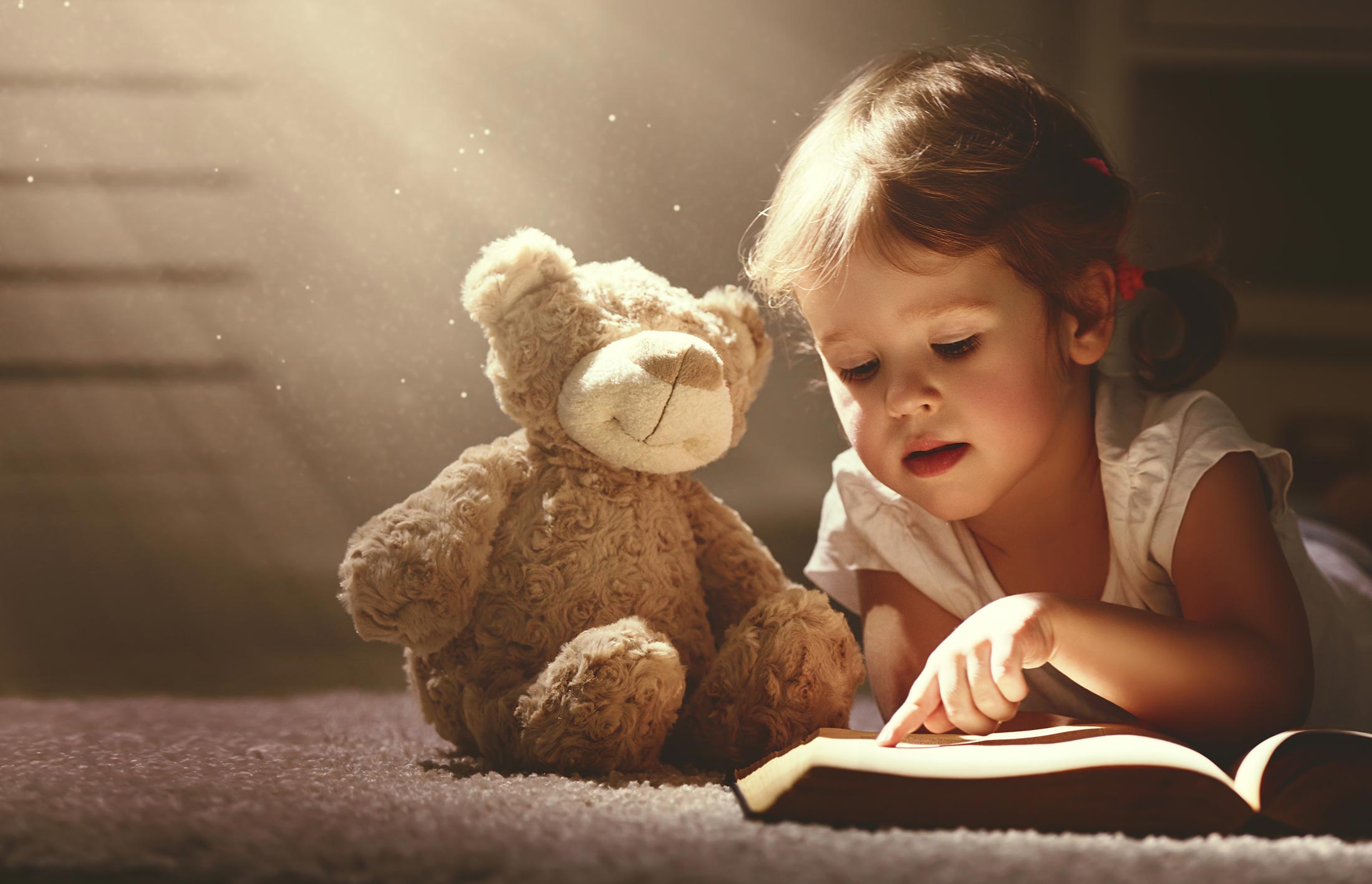 Child with a teddy bear reading a book